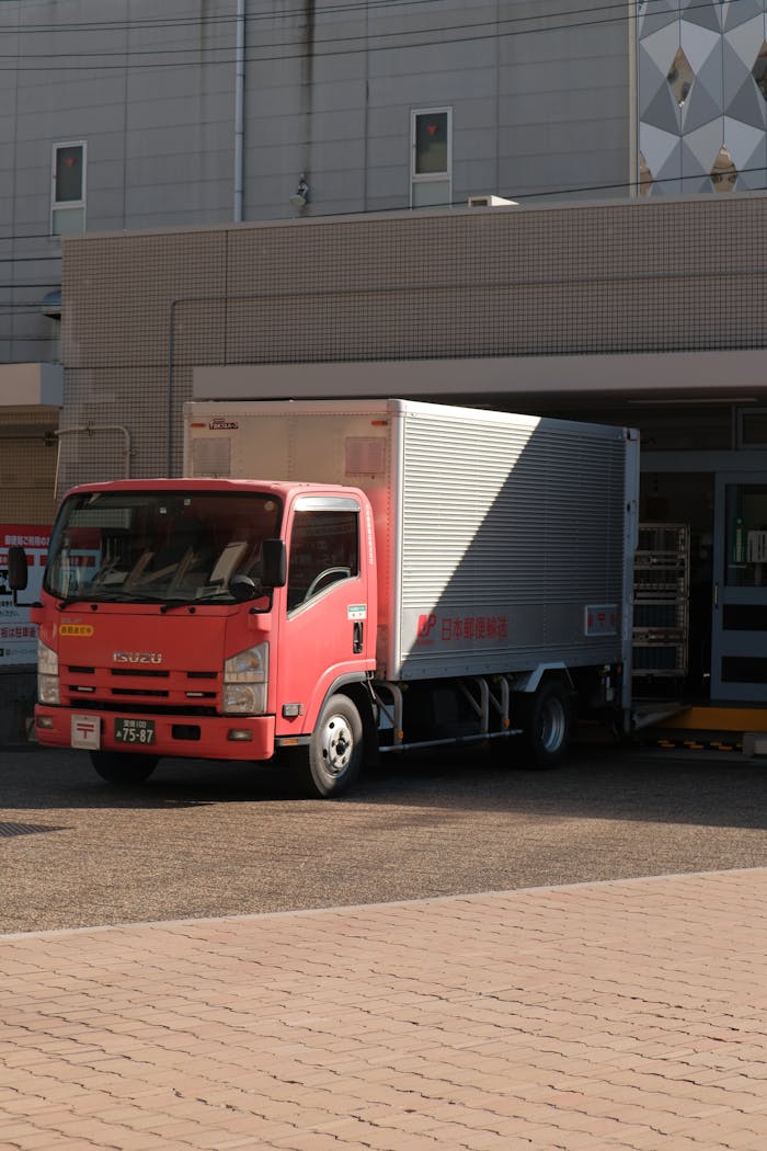 pexels-photo-18885403 A red delivery truck unloading goods at a warehouse on a sunny day in the city.